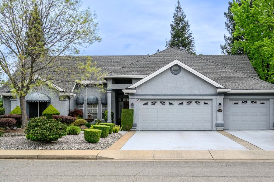 A home for sale in Redding with desert landscaping and a two car garage and trees behind the home