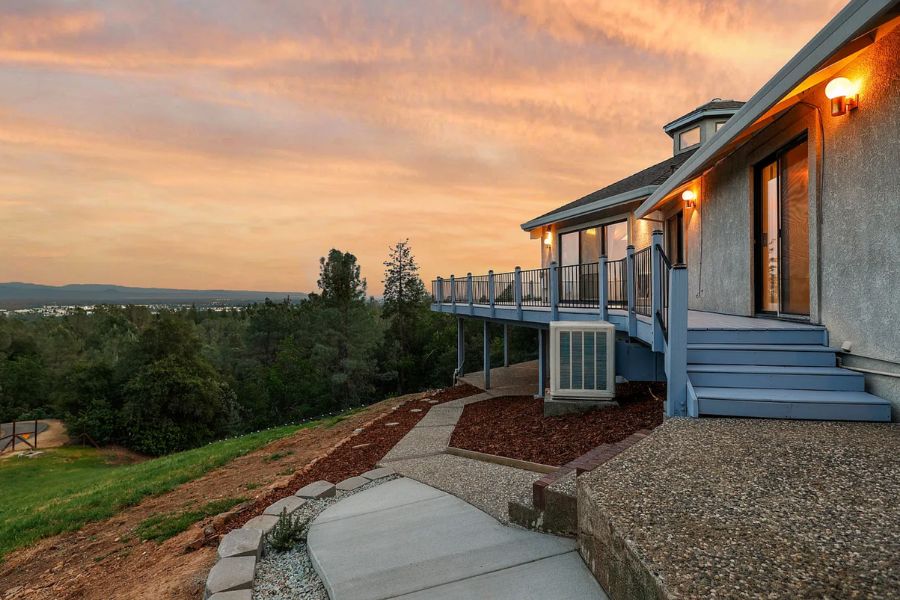 A redding home with a large wrap around deck showing views of mountains and trees at sunset